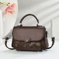 Detail van donkerbruine crossbodytas met vintage textuur en M-vormige metalen gesp - koffiekleur