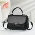 Detail van zwarte crossbody tas met ovale metalen M-gesp en een elegant handvat bovenop - Zwart