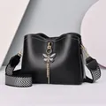 Modische schwarze Beuteltasche mit Schmetterlingsanhänger und gestreiftem Gurt auf Hintergrund - Schwarz