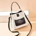Sac seau moderne en cuir blanc avec poche noire et bandoulière réglable sur podium - Blanc