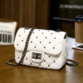 White quilted crossbody bag with metal studs and chain strap on a cafe table - White