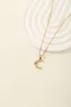 Detail of gold letter C pendant with blue stone and crystals on white geometric stand - Letter C