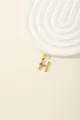 Detail of golden H letter pendant with blue and white crystals on beige background - Letter H