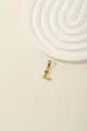 Detailed view of a gold letter L pendant with blue and white zircon stones on a beige background - L