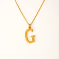 Macro detail of the textured 18k gold plated letter G pendant on a thin chain link - Letter G