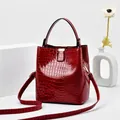 Rote glänzende Eimer-Handtasche mit Kroko-Prägung und goldenen Metallelementen - Rot