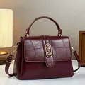 Detail der weinroten Handtasche mit Krokodilprägung und elegantem goldenem Metallverschluss - Burgunderrot