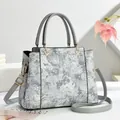 Elegante graue Handtasche mit weißer Blumenstickerei und goldenen Beschlägen von vorne - Grau