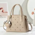 Beige quilted leather tote bag with rivets and heart charm, shown in a cozy home setting - Apricot