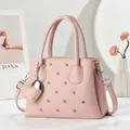 Pink lychee texture handbag with rivets, diamond stitching and heart charm on white background - Pink