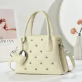 Detail of cream quilted handbag with heart patterns and silver stud accents - White