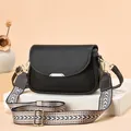 Close-up of black litchi pattern leather bag with gold hardware and striped strap - Black