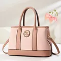 Pink woven tote bag with brown leather handles and gold metal logo shown from the front - Pink