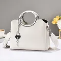 White lychee leather handbag with ring handle and heart charm on a decorative table - Off-white