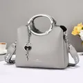 Light gray pebbled leather tote bag with round metal handles and decorative heart charm - Gray