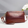 Detail van een bruine crossbodytas met krokodillenpatroon, goud logo en fijne riem - Bruin