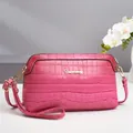 Detail van krokodillenstructuur op roze crossbodytas met goudkleurig logo en wit stiksel - Rozerood