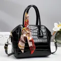 Elegante zwarte lakschelp tas met krokodillenprint, zijden sjaalhandvat en gouden accenten - Zwart