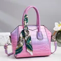 Nahaufnahme der Lackleder-Beuteltasche mit Krokoprägung, Seidenschal und Goldlogo - Lila