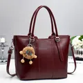 Detail view of burgundy bucket bag with vertical stitching and brown bear plush charm - Red