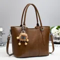 Dunkelbraune Leder-Beuteltasche mit Griffen und Plüsch-Anhänger auf weißem Tisch - Braun