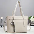 Chic cream leather tote bag with woven tassel and adjustable strap on a modern desk - White