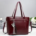 Detail of burgundy faux leather tote bag with lychee texture and woven pendant - Red