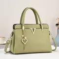 Détail du sac à main vert olive en cuir grainé avec logo V doré et pendentif cœur en perle - Vert