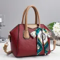 Detail of red lychee grain leather handbag with gold lettering and decorative silk scarf - Red