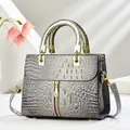 Detail of grey crocodile embossed texture on a chic trapezoid handbag with gold metal handles - Gray