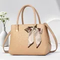 Detailed view of beige textured handbag with cylindrical handles and striped silk bow charm - Khaki