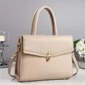 Beige pebble leather handbag with gold rotary lock shown from a professional studio angle - Apricot
