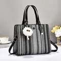 Stylish woven tote bag with leather handles and white plush charm on a clean background - Black