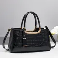 Close-up of black crocodile embossed handbag with golden U-shaped hardware and orchid decoration - Black