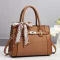 Dettaglio di borsa marrone con texture intrecciata e foulard decorativo sul manico - Marrone