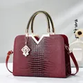 Detail of burgundy crocodile pattern handbag with golden V-accent and woven handles - Wine Red