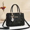 Elegant black snake pattern tote bag with gold logo and pearl bow charm on beige background - Black