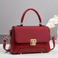 Detail of red crossbody bag featuring textured woven flap and gold square push lock closure - Red