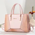 Detail der rosa Handtasche mit Krokodilprägung und goldenem Logo auf glattem Leder - Rosa