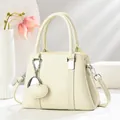 Gros plan du sac coquillage en cuir litchi beige avec ferrures argentées et pendentif - Blanc