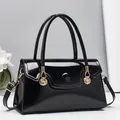 Close-up of black patent leather handbag featuring golden shell pendants and metal hardware - 30cm x 12cm x 13cm / Black