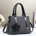 Détail de la texture tricotée d'un sac à main gris foncé avec poignée noire et breloque fleur - Noir