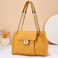 Macro shot of yellow quilted shoulder bag featuring gold chain strap and metal lock closure - Earthy Yellow
