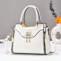 Elegant ivory faux leather handbag with golden swan hardware and pearl charms shown on a desk - White