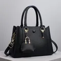 Black pebble leather tote bag with gold hardware and mini bag charm on a stone platform - Black