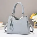 Detalle de bolso de mano gris claro en cuero granulado con herrajes plateados y colgante - Azul