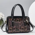 Detail of leopard print pillow bag with black patent leather handles and gold hardware - Coffee