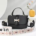 Black textured crossbody bag with gold H clasp and boho floral wide strap in chic home setting - Black