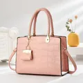 Detail der rosa Handtasche mit Krokodil-Prägung, Webgriff und Mini-Taschenanhänger - Rosa