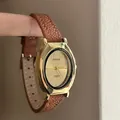 Elegant women's quartz watch with gold oval case and brown leather strap on warm background - Coffee